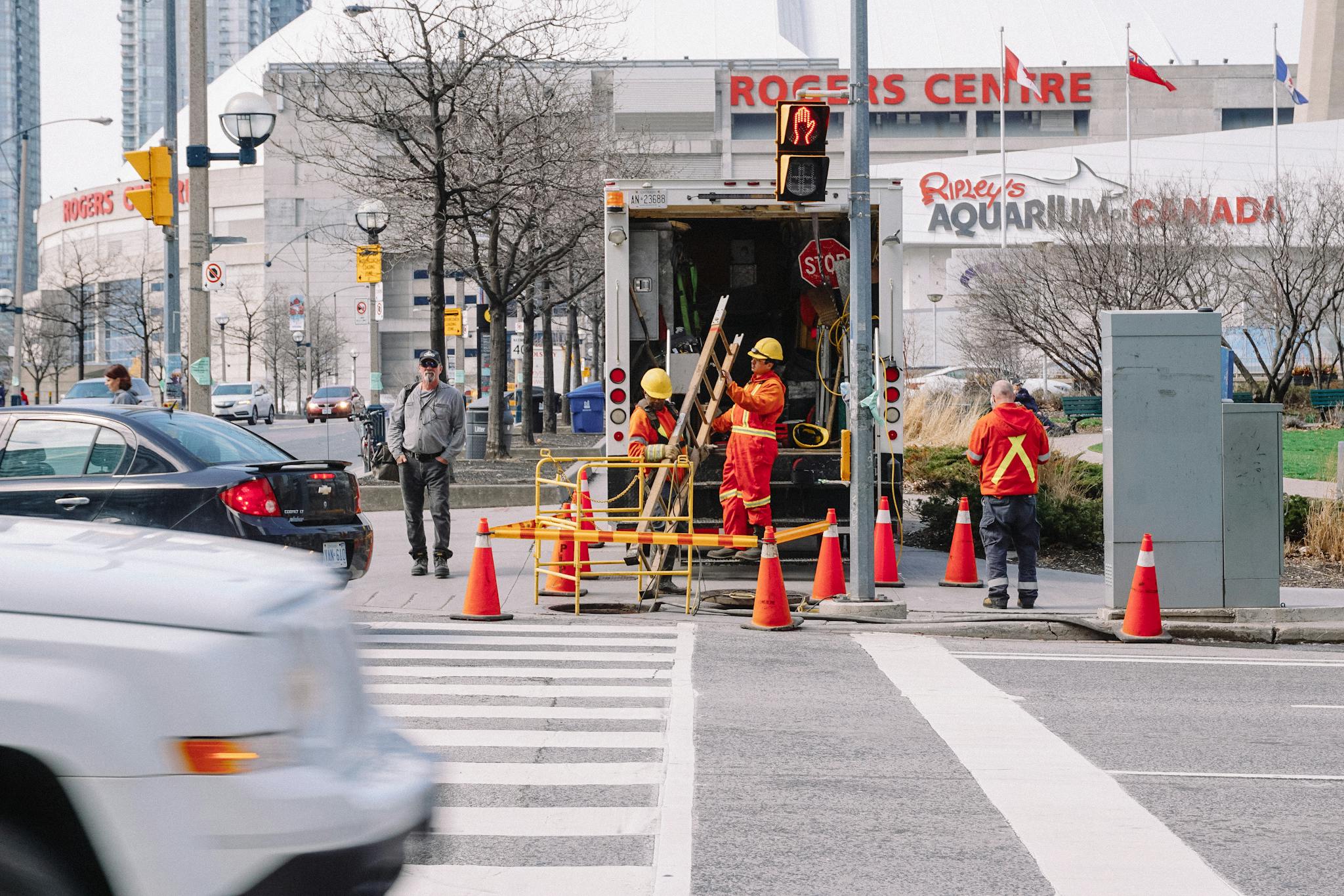Full body of workers in red uniforms and yellow helmets carrying wooden ladder in street near automobile road